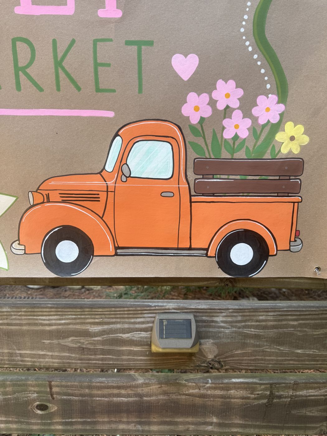 Close-up of a hand-painted orange pickup truck carrying pink flowers
