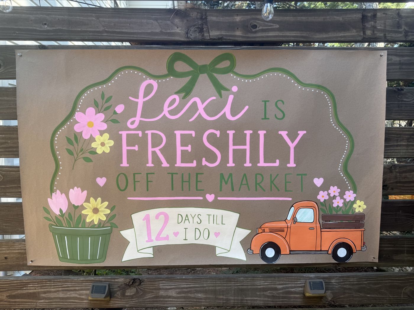Hand-painted banner reading Lexi is freshly off the market, with a flower basket and an orange pickup truck
